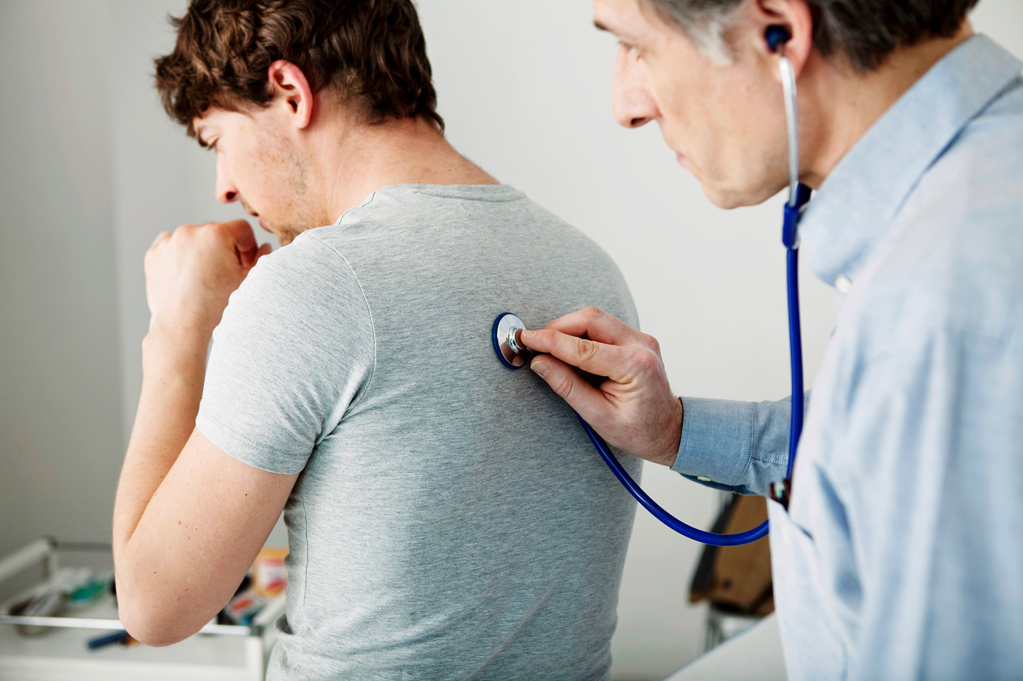 Man coughing while a clinician holds a stethoscope against his back